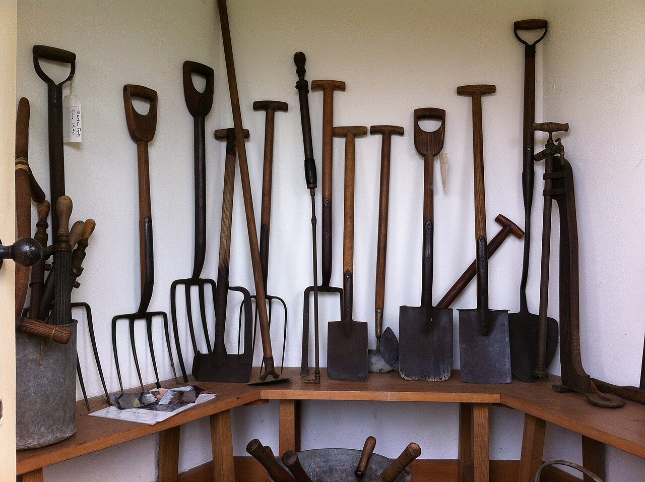 A garden tool room with a wooden bench and several long-handled tools against the surrounding walls